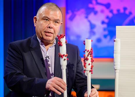 Jonathan Van-Tam holding up some props of white sticks with red bobbles on them