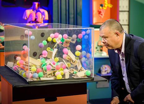 Jonathan Van-Tam looking at a perspex box filled with colourful ping pong balls and mouse traps that are setting each other off