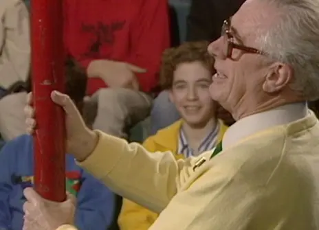 Charles Taylor holding a large red metal rod, with children smiling in th ebackground of the Ri theatre