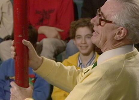 Charles Taylor holding a large red metal rod, with children smiling in th ebackground of the Ri theatre