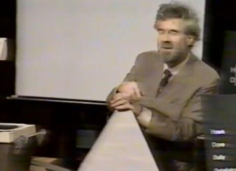 Christopher Zeeman leaning his hands on a large white cardboard triange in the Ri theatre