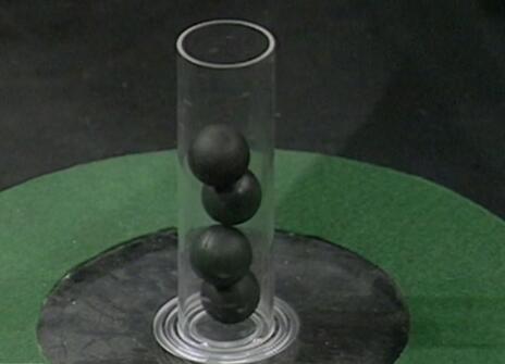 A glass cylinder holding four black balls
