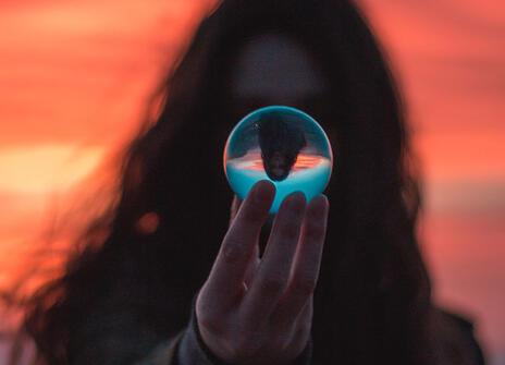 a silhouette of a long haired person holding up a glass ball in which the same person is appearing upside down