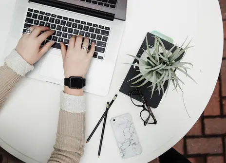 A woman's hands typing on a laptop, next to a shrub