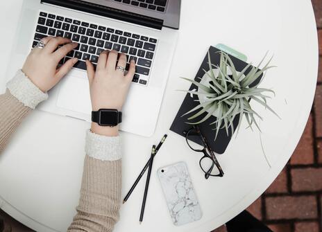 A woman's hands typing on a laptop, next to a shrub