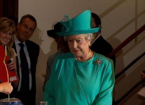 Her Majesty the Queen wearing a green dress and hat, watching a science demonstration