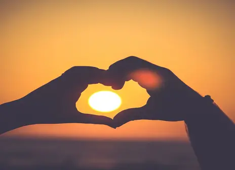 Two hands making heart around sunset 