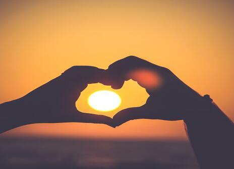 Two hands making heart around sunset 
