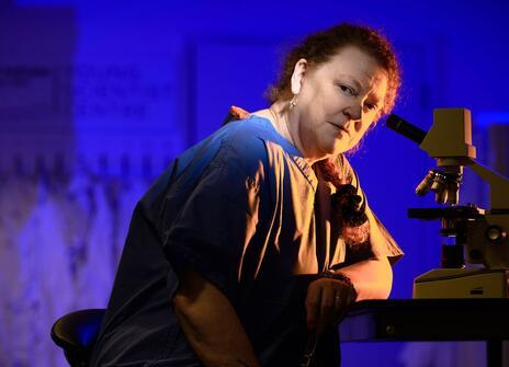 Sue Black, a white woman, is in a lab with a microscope, she's looking at the camera