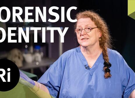 Professor Dame Sue Black, dressed in blue scrubs, has her hands slightly raised. Overlayed are the words 'FORENSIC IDENTITY' along with the Royal Institution Logo.