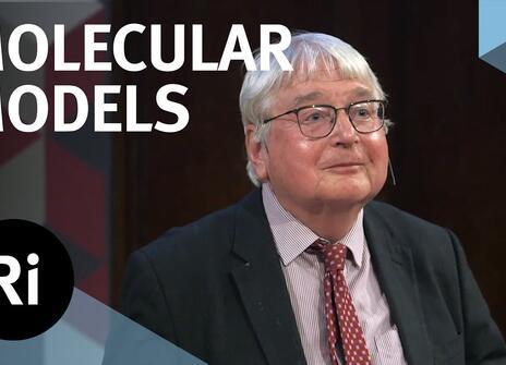 A presenter stands on a stage. The words 'MOLECULAR MODELS' are written above, along with the Royal Institution Logo.