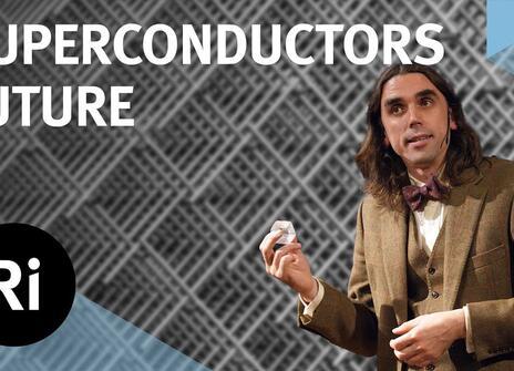 A presenter in a tweed jacket stands, holding a small white object. Above them is written 'SUPERCONDUCTORS FUTURE' along with the logo of the Royal Institution.