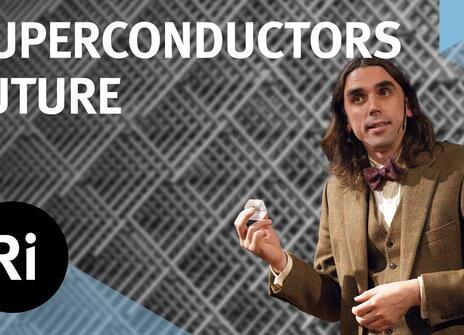 A presenter in a tweed jacket stands, holding a small white object. Above them is written 'SUPERCONDUCTORS FUTURE' along with the logo of the Royal Institution.