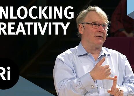 A presenter stands on a stage with his hands slightly raised. The words 'UNLOCKING CREATIVITY' are written above, along with the Royal Institution Logo.