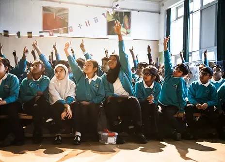 Children at a science shows enthusiastically raise their hands to volunteer