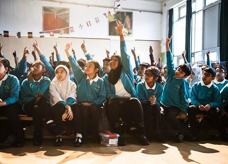 Children at a science shows enthusiastically raise their hands to volunteer