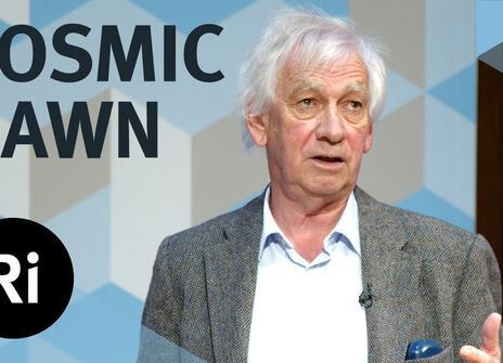 The speaker faces the front of the stage, hands slightly raised. Overlayed are the words 'COSMIC DAWN' alongside the Royal Institution's logo.