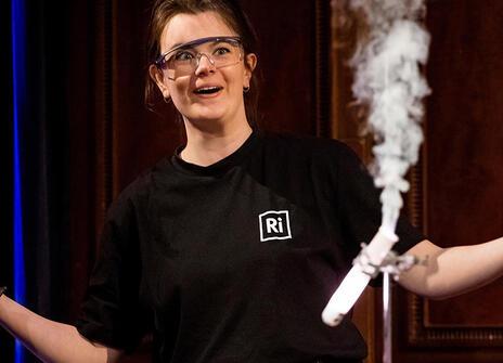 A demonstration with lots of smoke. Behind it, a woman stands with her arms open, smiling.