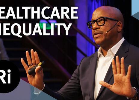 A presenter stands on a stage with his hands slightly raised. The words 'HEALTHCARE INEQUALITY' are written above, along with the Royal Institution Logo.