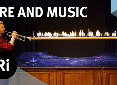 Anna Ploszajski blows a trumpet onto a fire contraption in the Royal Institution theatre, to demonstrate the conversion of sound waves.