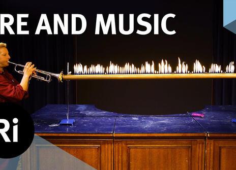 Anna Ploszajski blows a trumpet onto a fire contraption in the Royal Institution theatre, to demonstrate the conversion of sound waves.