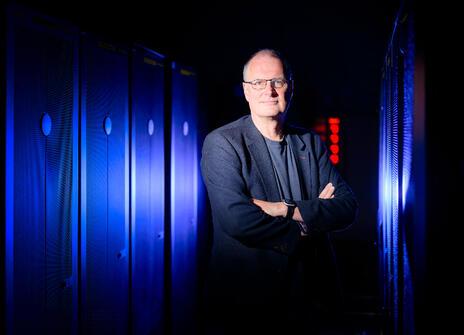 Professor Mike Wooldridge looks into the camera with a blue lit background behind him