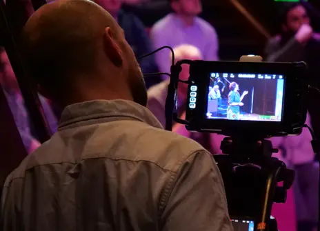 A man looks through a camera screen at the audience at an Ri talk
