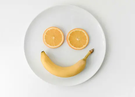 Two orange slices and a banana on a plate, making a smiley face shape
