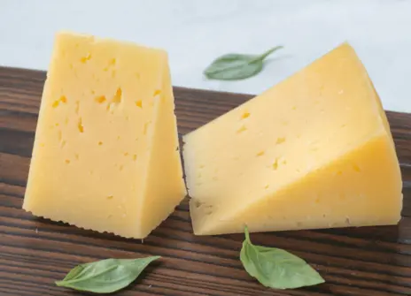 Two pieces of cheese on top of a wooden cutting board.