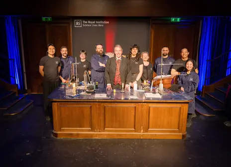 A group of people in black t shirts stood behind a wooden desk