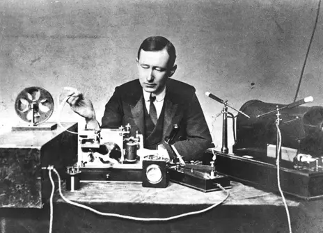 Marconi at a table, sitting behind his equipment in 1901