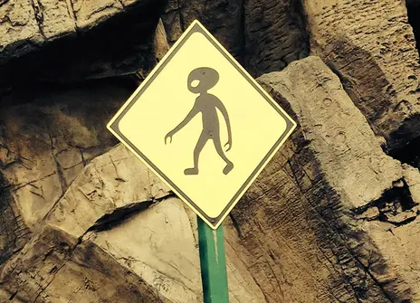 A diamond-shaped yellow sign with a silhouette of an alien walking