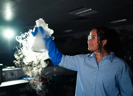 A woman holding a flask, its contents bubbling away in smoke