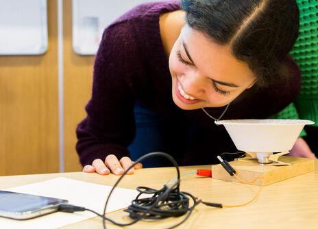 young woman looks at a jumble of wires and electronic parts