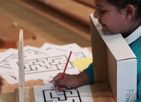 a girl in school uniform is tryin to solve a maze by looking at its reflection in the mirror