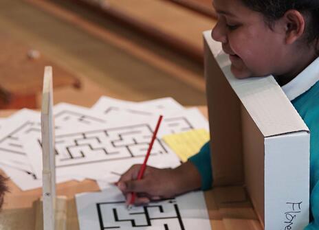 a girl in school uniform is tryin to solve a maze by looking at its reflection in the mirror