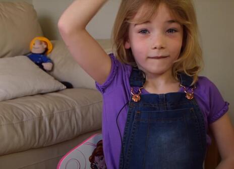small girl in dungarees with one hand on her head and another on her belly