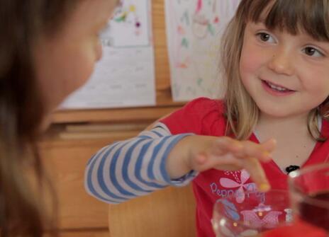 a young girl is running her finger over the rim of a glass while smiling at her mother