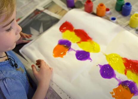 a young girl is looking at a paper covered in paint splatters