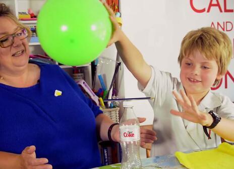 a woman with glasses leans away as a young boy holds up a balloon in one hand