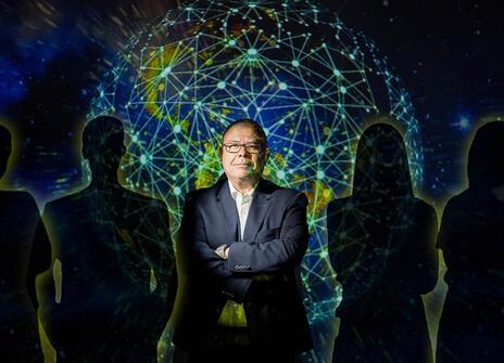 Jonathan van Tam with his arms crossed and a projection of a globe overlaying him, he's surrounded by silhouettes of six people