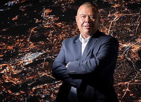 Jonathan Van-Tam with his arms crossed in front of an aerial view of a city at night with bright lights