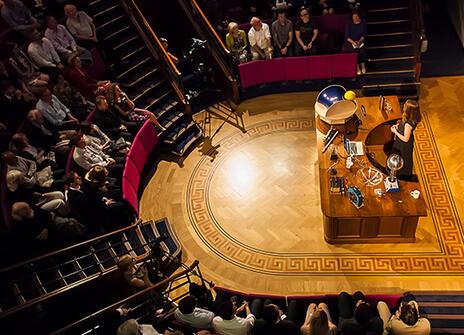 Ri lecture theatre from above, a person is presenting a talk on stage, the audience watches