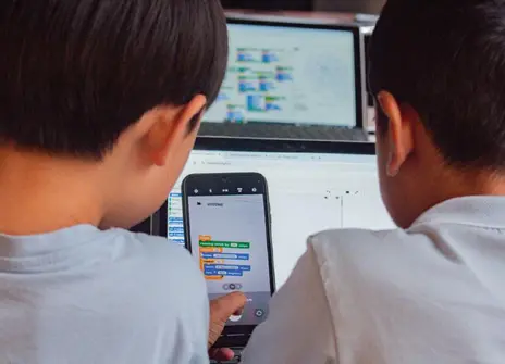 Two children stare at a screen with lines of code