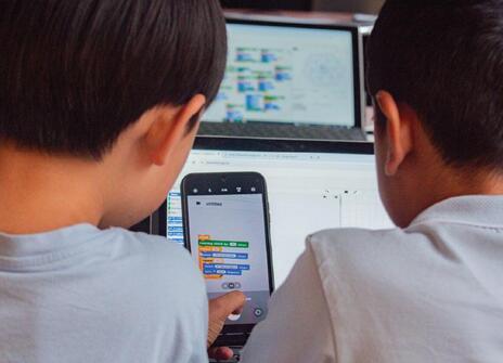 Two children stare at a screen with lines of code