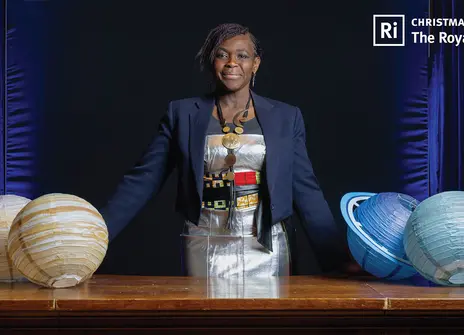 Maggie Aderin behind a desk with model planets atop it