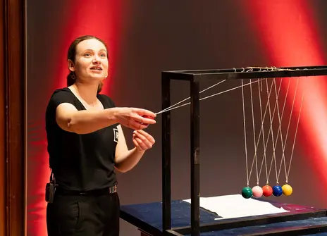 A woman about to activate a Newton's cradle with colourful balls