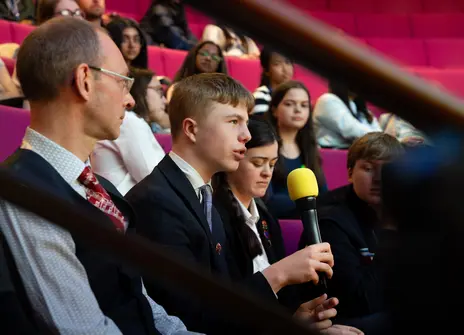 A student speaking into a microphone in a theatre setting