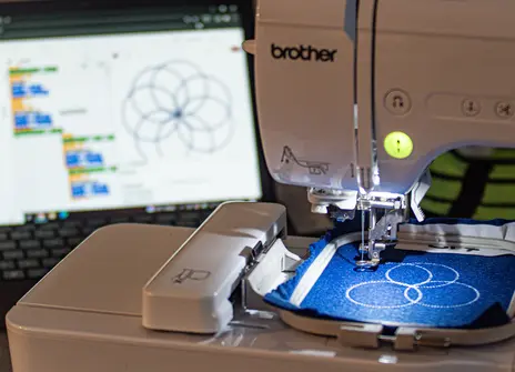 Embroidery machine stitching a pattern that can be seen on a screen behind