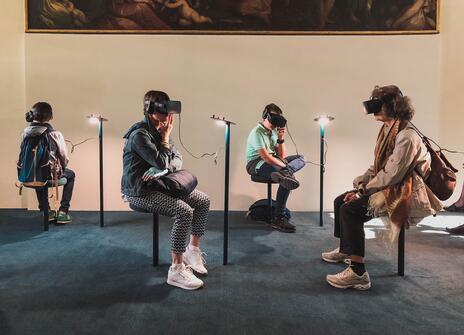 Four people are sat in a room. They are each wearing a virtual reality headset. 